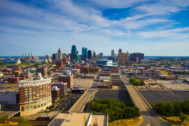 Aerial view of downtown Kansas City, Missouri on a summer morning, looking north from Crown Center across rooftops and a road viaduct toward the downtown towers.